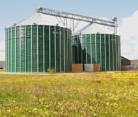 Biogas-Fermenter vor Blumenwiese - Symbolbild für Biomethan.