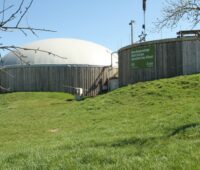 Fermenter einer Biogasanlage auf einem grünen Wiesenhügel.