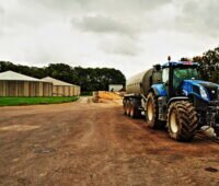 Landwirtschaftlicher Hof mit Biogasfermentern im Hintergrund und einem Traktor im Vordergrund.