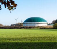 Biogasanlage in grüner Landschaft mit Windkraftanlagen im Hintergrund