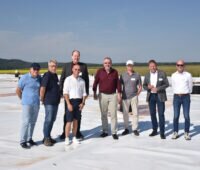 Personengruppe mit u.a. Klaus Vajen, Helgo Schütze, Christian Stadler auf der Kunststoff-Abdeckung des Erdbecken-Wärmespeichers