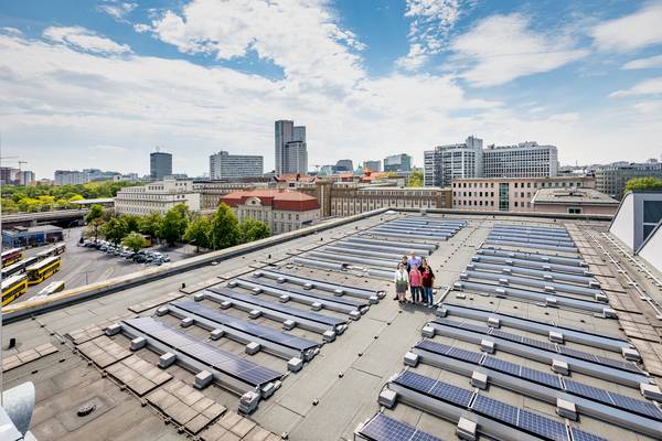 Bürger stehen zwischen Solarmodulen auf einem Flachdach in einer Stadt.