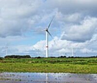 Windpark vor blauem Himmel und Wolken und großen Regenpfützen.