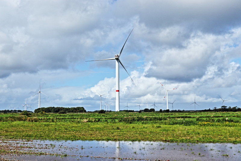 Windpark vor blauem Himmel und Wolken und großen Regenpfützen.