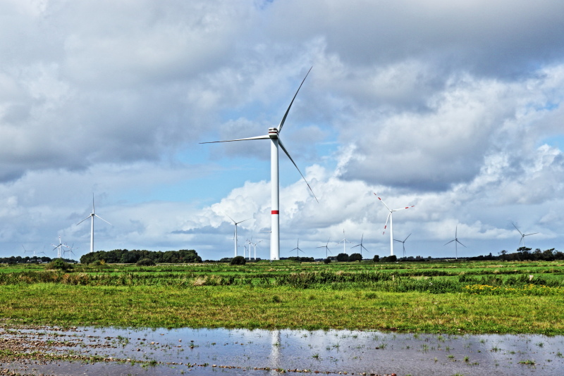 Windparks können künftig für mehr Systemsicherheit sorgen wie hier einer Bürgerwindpark vor blauem Himmel und Wolken und großen Regenpfützen.r
