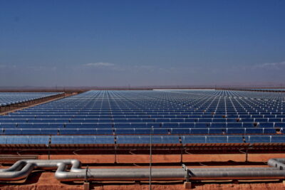 Parabolrinnen-Kollektorfeld auf roter Erde, in der Ferne eine Gebirgskette - konzentrierende Solarthermie.