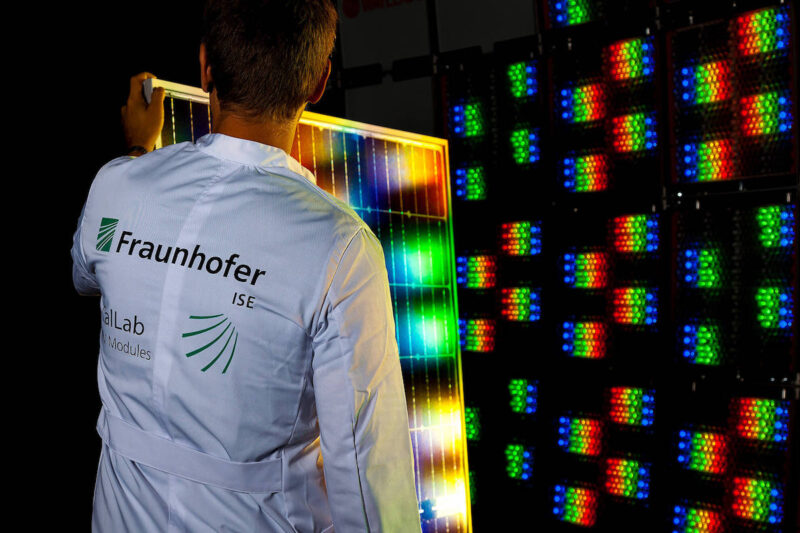 Mitarbeiter des Fraunhofer ISE hält ein PV-Modul vor einen multispektralen Sonnensimulator mit roten, grünen und blauen LEDs.