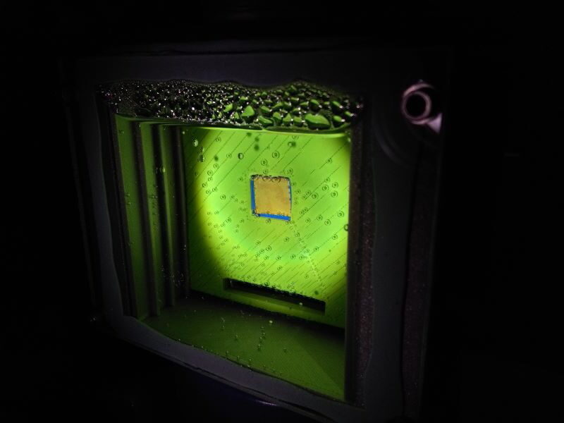 Ein grün schimmernder Wasserbehälter mit einem quadratischen goldenen Katalysator in der Mitte umgeben von Sauerstoffbläschen.