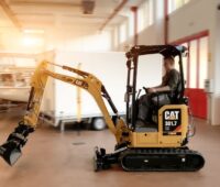 Ein elektrischer Minibagger vob Caterpillar fährt in einer Industriehalle.