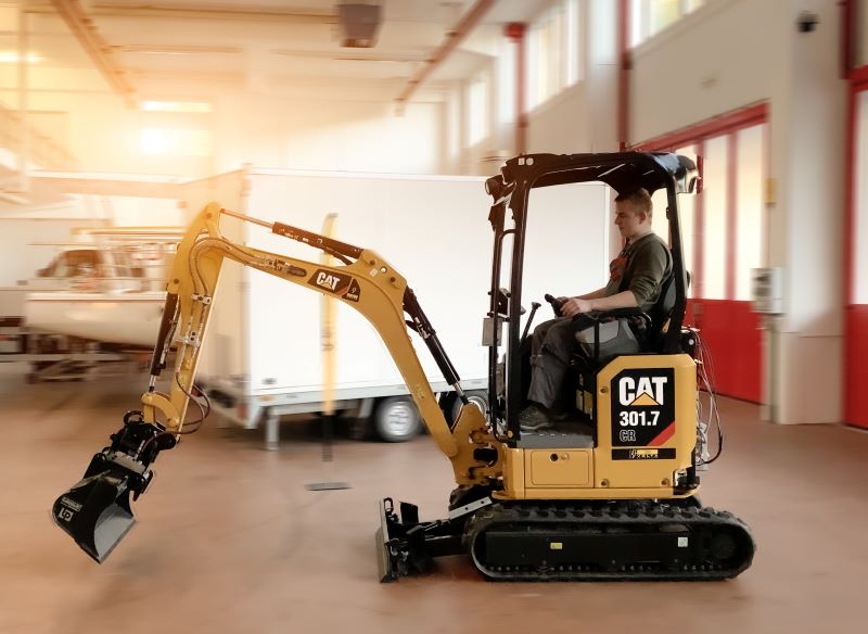 Ein elektrischer Minibagger vob Caterpillar fährt in einer Industriehalle.