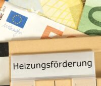 Mehrere Euro-Geldscheine - gelb, grün, braun - liegen unter einer beigen Akte mit der Aufschrift „Heizungsförderung“ und symbolisieren die staatliche Förderung für den Heizungstausch.