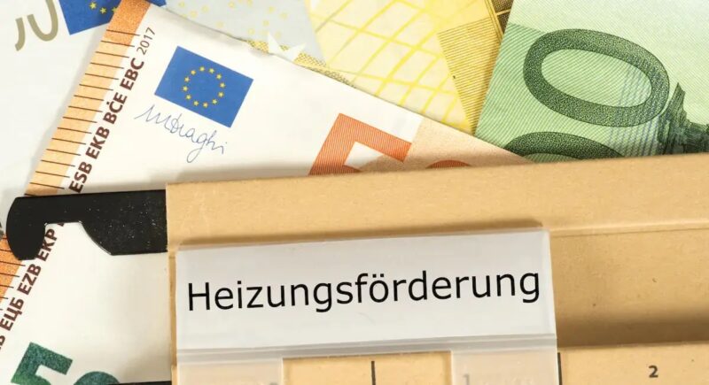 Mehrere Euro-Geldscheine - gelb, grün, braun - liegen unter einer beigen Akte mit der Aufschrift „Heizungsförderung“ und symbolisieren die staatliche Förderung für den Heizungstausch.