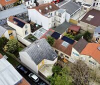 Blick auf mittelgroße Wohnhäuser mit Giebeldächern, zwei davon mit PVT-Kollektoren.