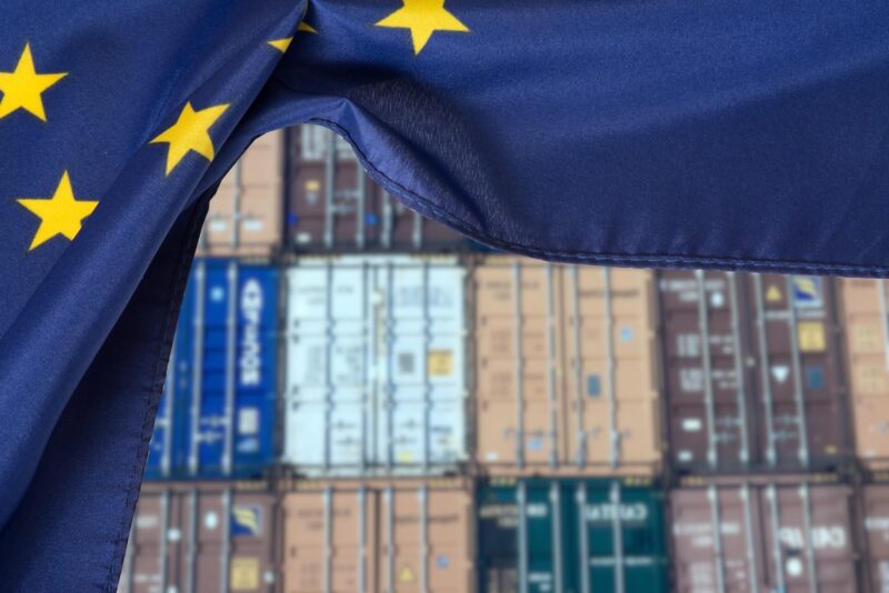 Container gestapelt, davor EU-Flagge, Symbol für Schutzmaßnahmen für Solarindustrie