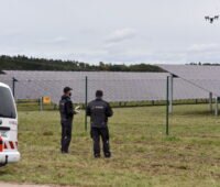 Zwei Männer steuern eine Drohne über einem PV-Feld.