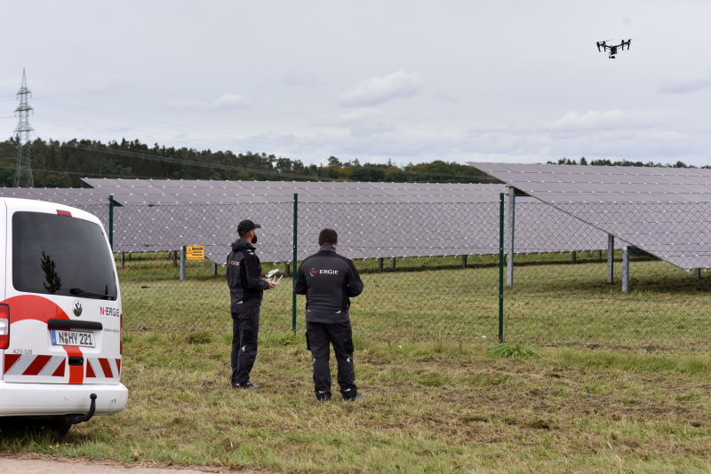 Zwei Männer steuern eine Drohne über einem PV-Feld.