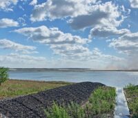 Blick über einen künstlichen Binnensee mit Kohle-Kühltürmen am Horizont sowie Windkraftanlagen