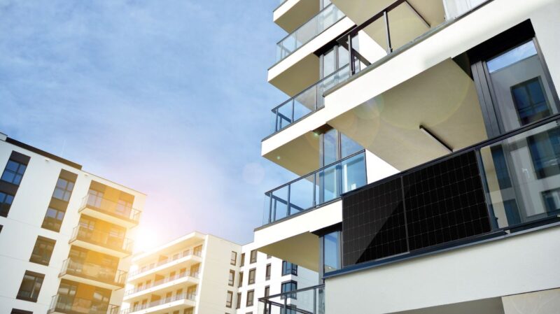 Schwarzes Solarmodul an einem Balkon in einer modernen Appartementsiedlung.