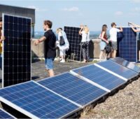Personen arbeiten auf dem Flachdach eines Hochhauses an Steckersolaranlagen.