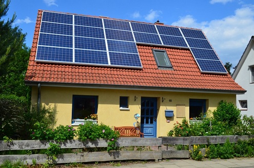 Foto eines Ein-familienhauses mit Garten und Bäumen. Auf dem Dach befindet sich eine PV-Anlage.