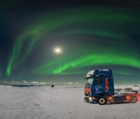 Winterlandschaft am Nordkapp: im Hintergrund grünes Polarlicht, im Vordergrund ein Elektro-LKW