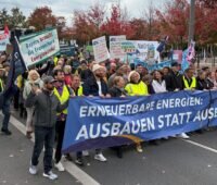 Demonstrierende halten ein großes Banner mit der Aufschrift „Erneuerbare Energien: Ausbauen statt ausbremsen!“. Dahinter tragen weitere Teilnehmende Plakate und Fahnen.