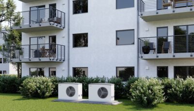 Im Bild ein Mehrfamilienhaus mit Wärmepumpe, neuer Praxis-Leitfaden für Wärmepumpen in Mehrfamilienhäuser der Dena.