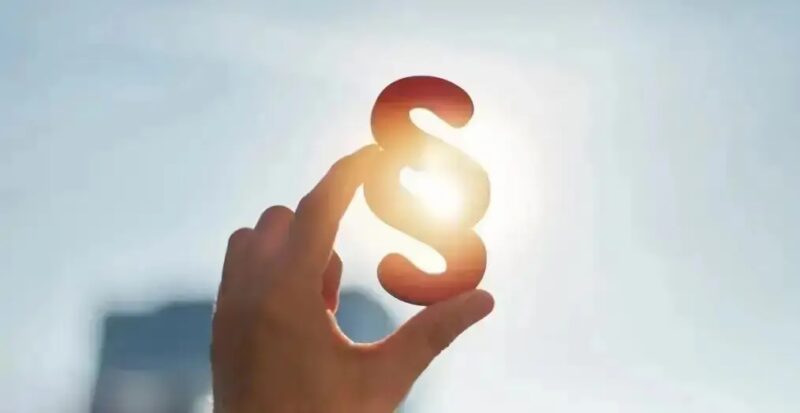 Eine Hand hält ein Paragrafenzeichen in die Sonne.