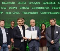 Mehrere Projektbeteiligte stehen auf einer Bühne und präsentieren den Förderbescheid für das Projekt DIGIBATT360. Im Hintergrund sind die Namen weiterer GreenTech-Förderprojekte an einer grünen Wand eingeblendet.