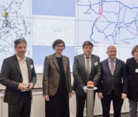 Drei Männer und zwei Frauen hinter rotem Knopf und vor Karte des Energiesystems - Start für den digitalen Zwilling