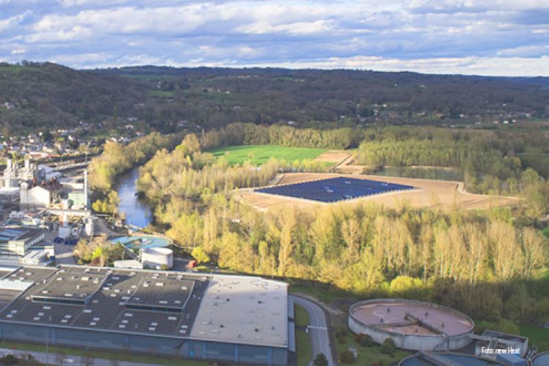 Eine große Solarthermieanlage umgeben von Feldern am französischen Fluss Dordogne. Auf der anderen Seite des Flusses ein Industriebetrieb.