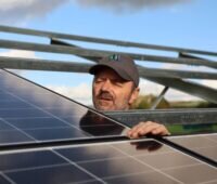 Installateuer lugt zwischen Solarmodulen hervor, die auf Unterkonstruktion ruhen.