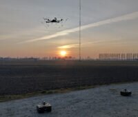 Eine Drohne startet zum Sonnenuntergang vor einer Windenergieanlage in den Himmel.
