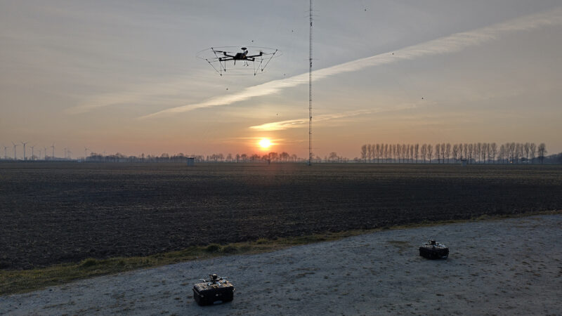 Eine Drohne startet zum Sonnenuntergang vor einer Windenergieanlage in den Himmel.