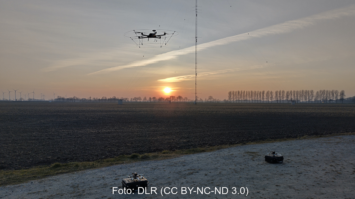 Eine Drohne startet zum Sonnenuntergang vor einer Windenergieanlage in den Himmel.