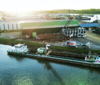 Aus der Vogelperspektive liegt ein Seilbaggerschiff am Pier im aufgehenden Sonnenlicht.