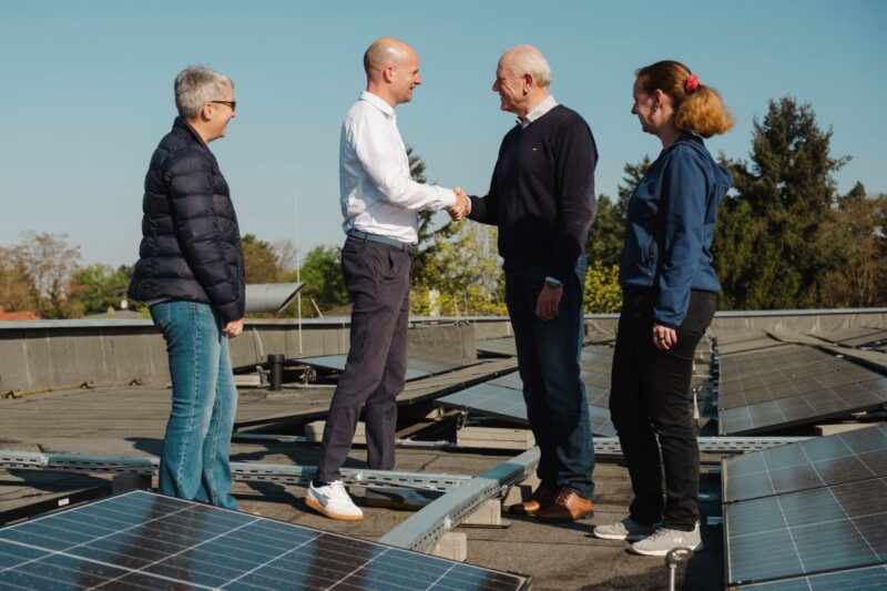 Vier Personen bei der Handschlag-Übergabe von Aufdach-PV-Anlagen auf dem Dach einer Kita in Berlin.