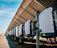 Rückseite mehrerer Solarmodule in einem Solarpark. An den Modulen sind Wechselrichter montiert, die den erzeugten Gleichstrom in Wechselstrom umwandeln.
