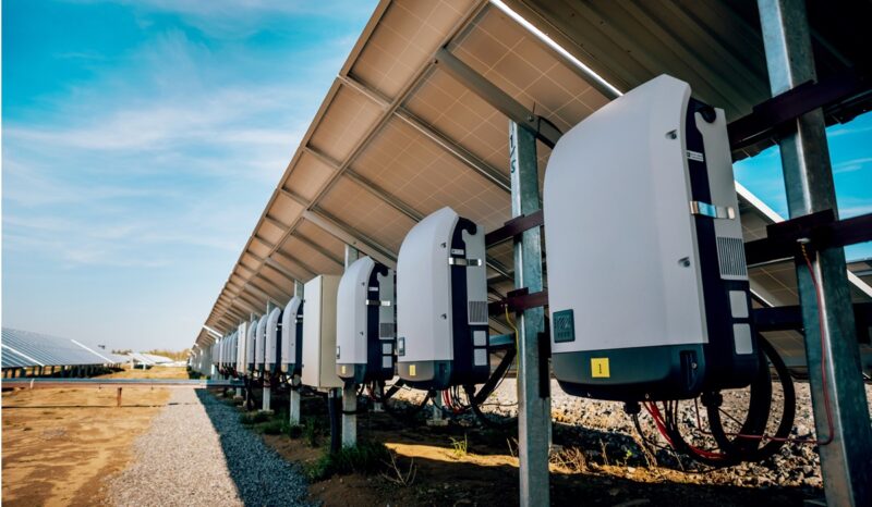 Rückseite mehrerer Solarmodule in einem Solarpark. An den Modulen sind Wechselrichter montiert, die den erzeugten Gleichstrom in Wechselstrom umwandeln.