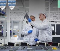 Zwei Q-Cells-Mitarbeiter halten eine Solarzelle hoch, am Bildrand die Logos für Top Brand PV und QCells