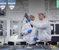 Zwei Q-Cells-Mitarbeiter halten eine Solarzelle hoch, am Bildrand die Logos für Top Brand PV und QCells