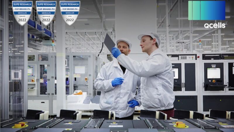 Zwei Q-Cells-Mitarbeiter halten eine Solarzelle hoch, am Bildrand die Logos für Top Brand PV und QCells