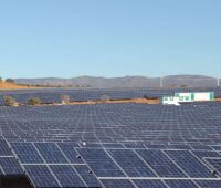 PV-Freifläche auf sandigem Boden im Vordergrund. Im Hintergrund blauer Himmel und Berge