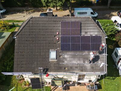 Luftaufnahme eines freistehenden Einfamilienhauses, auf dem gerade eine PV-Anlage montiert wird.