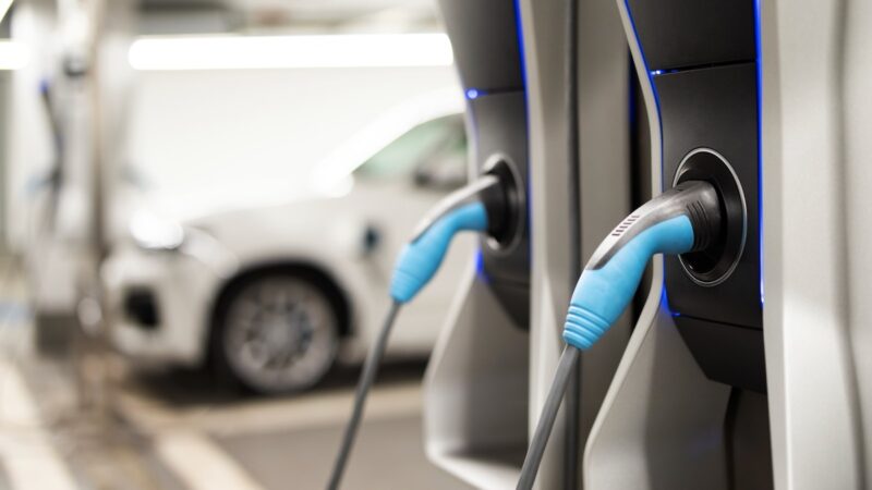 Zwei Ladepunkte an einer Ladesäule, im Hintergrund eine weitere Ladesäule mit einem E-Auto