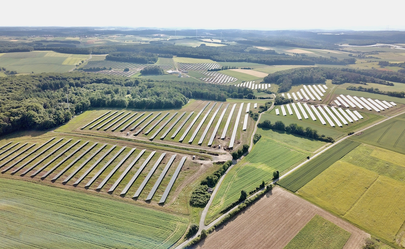 Luftbild einer Photovoltaik-Freiflächen-Anlage aus mehreren Teilfeldern zwischen Wiesen und Wäldern.