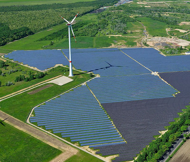 Luftaufnahme eines Freiflächensolarparks mit einer Windkraftanlage