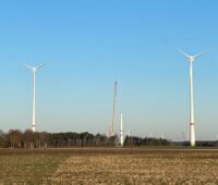 Vier Windenergie-Anlagen von Enercon hinter einem Acker, vor einem Wald