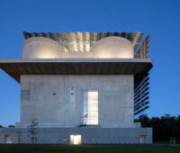 Ein alter Flakbunker bestrahlt gegen dunklen Himmel, an den Seiten der Fassaden Solarkollektoren.