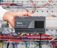Eine hand hält den Energiemanager Enbas vor den Kablen udn Steckern eines Schaltschrankes.